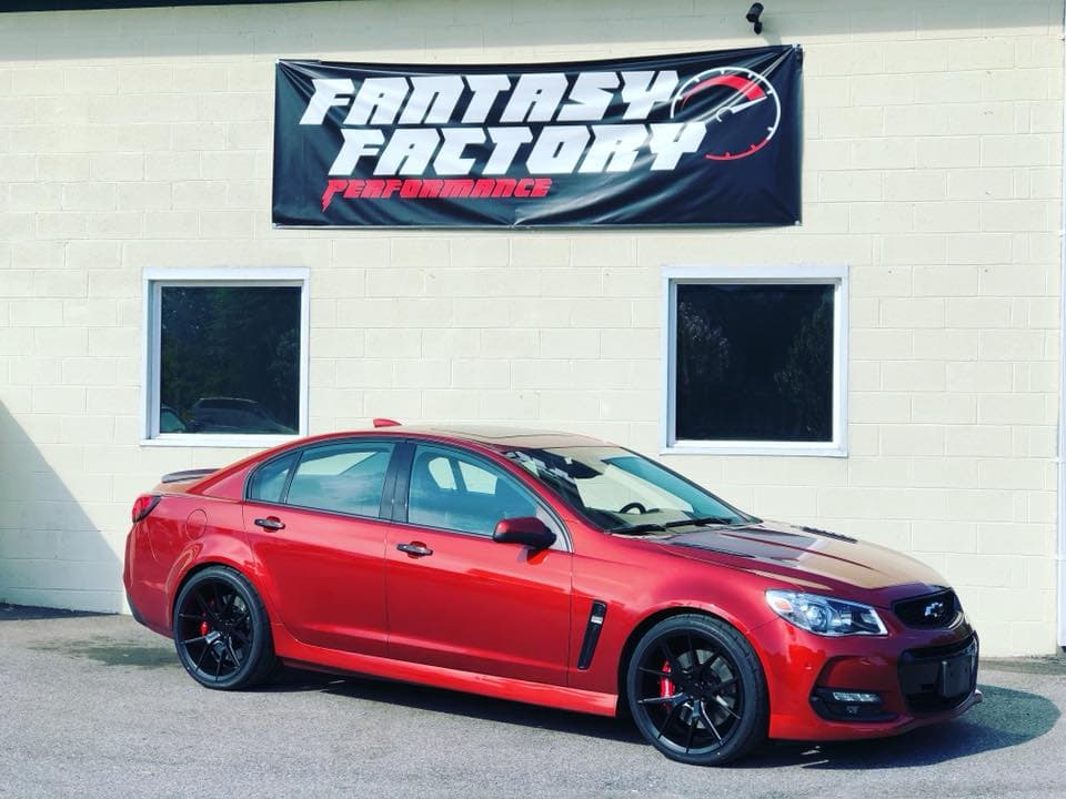 Photograph of a Chevy SS parked in front of the shop, with the shop's banner logo prominently displayed on the building in the background, setting the scene for a car enthusiast's ideal shopping destination.